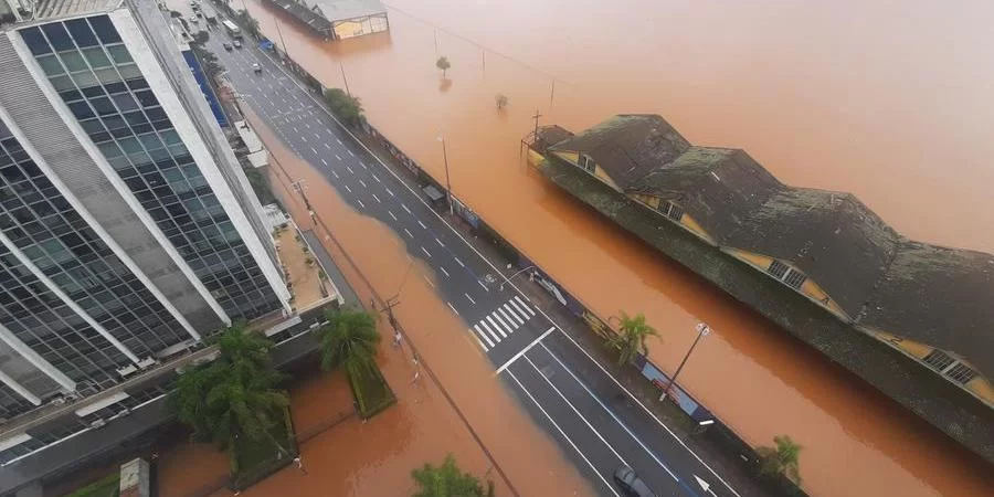Vista aérea de uma avenida e prédios submersos pela água barrenta de uma enchente.