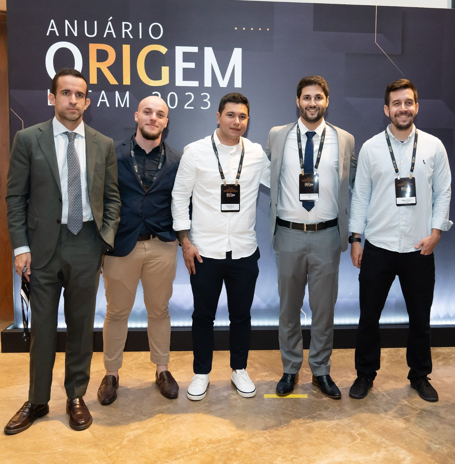 Cinco integrantes da equipe da Nomos posando diante do painel do Anuário ORIGEM LATAM 2023.