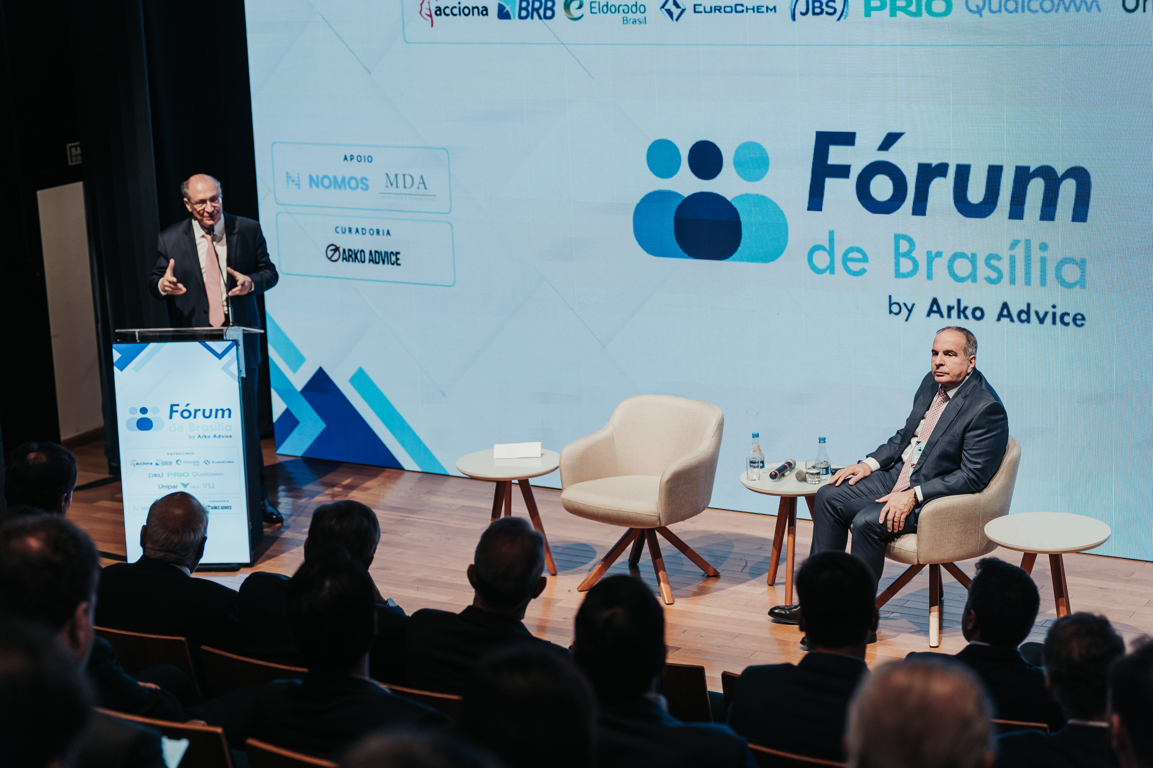 Palestrante ao púlpito do Fórum de Brasília by Arko Advice, diante da plateia e do palco com poltronas.