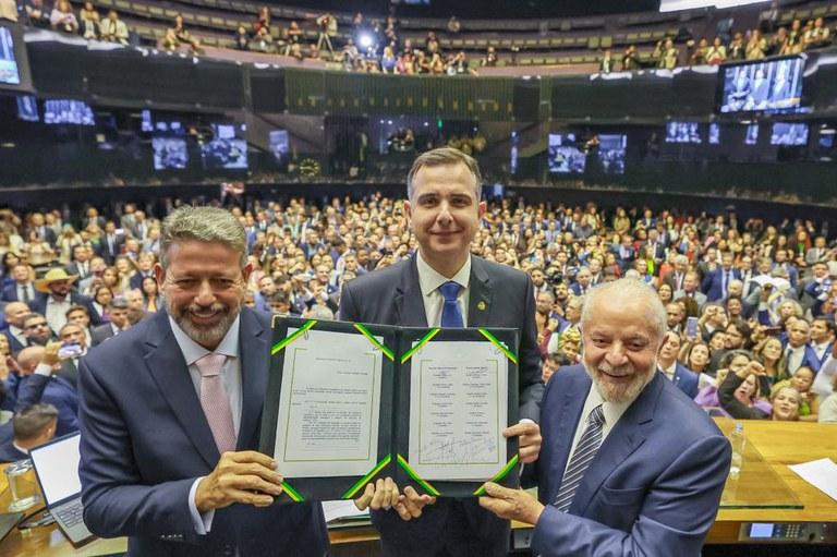 Arthur Lira, Rodrigo Pacheco e Lula exibem o texto da reforma tributária promulgada diante do plenário lotado.